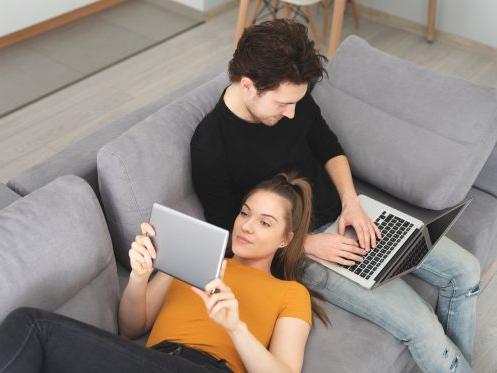 一对夫妇坐在沙发上，用家里的wi-fi信号连接他们的无线设备. 光纤和无线网络都适合他们的wi-fi需求.